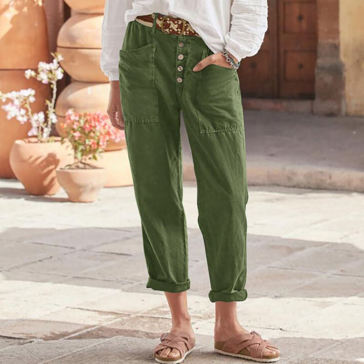 Green casual pants with button front and rolled cuffs, worn with a white top and sandals in a bright courtyard.