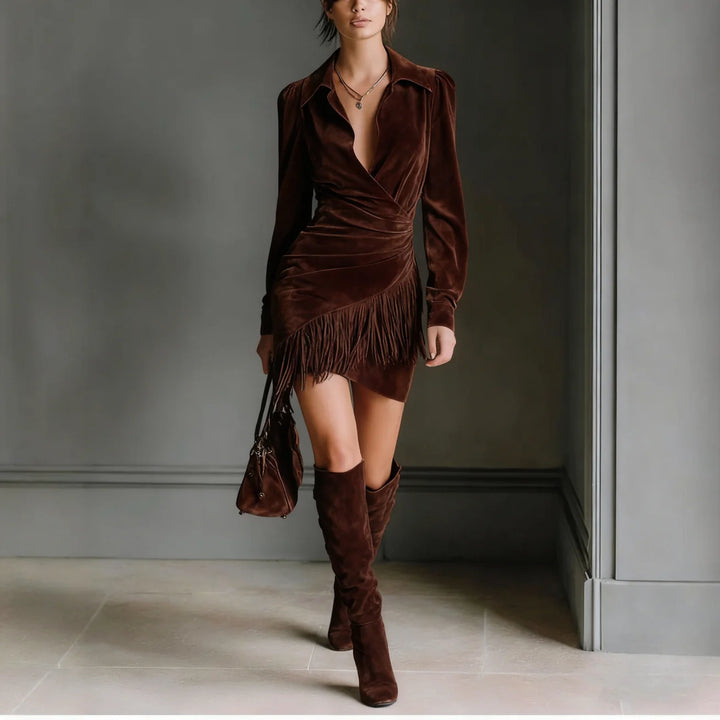 Chic woman wearing a brown mini dress with fringe detail and knee-high boots, in a sophisticated indoor space.