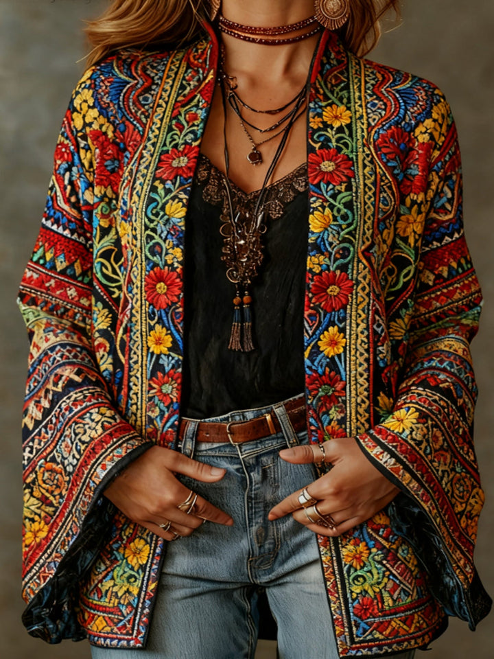 Colorful floral embroidered kimono cardigan worn by a woman with layered necklaces and jeans, studio backdrop.