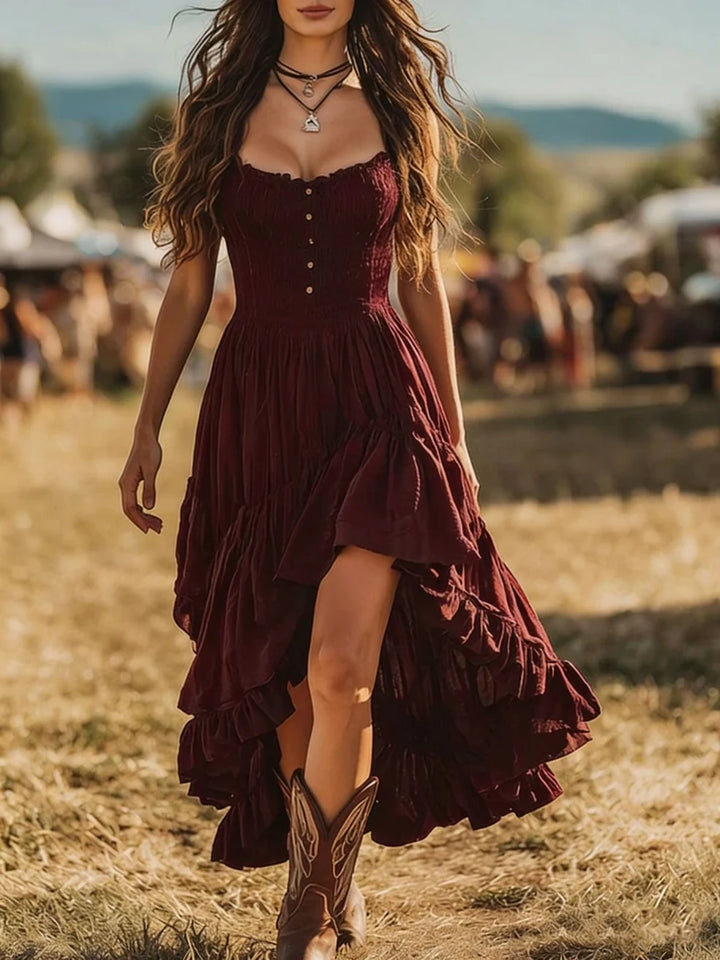 Woman in a burgundy maxi dress with tiered skirt and cowboy boots at an outdoor festival.