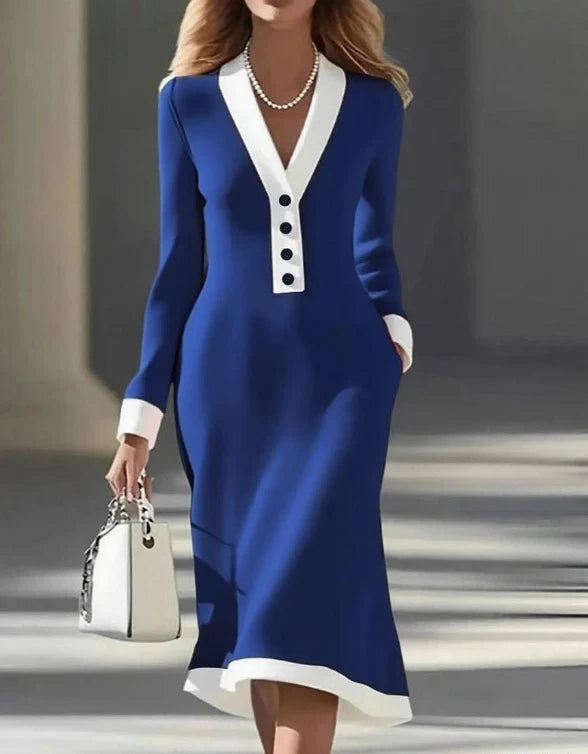 Blue long-sleeve dress with white trim and buttons, accessorized with a pearl necklace and white handbag, in an urban environment.