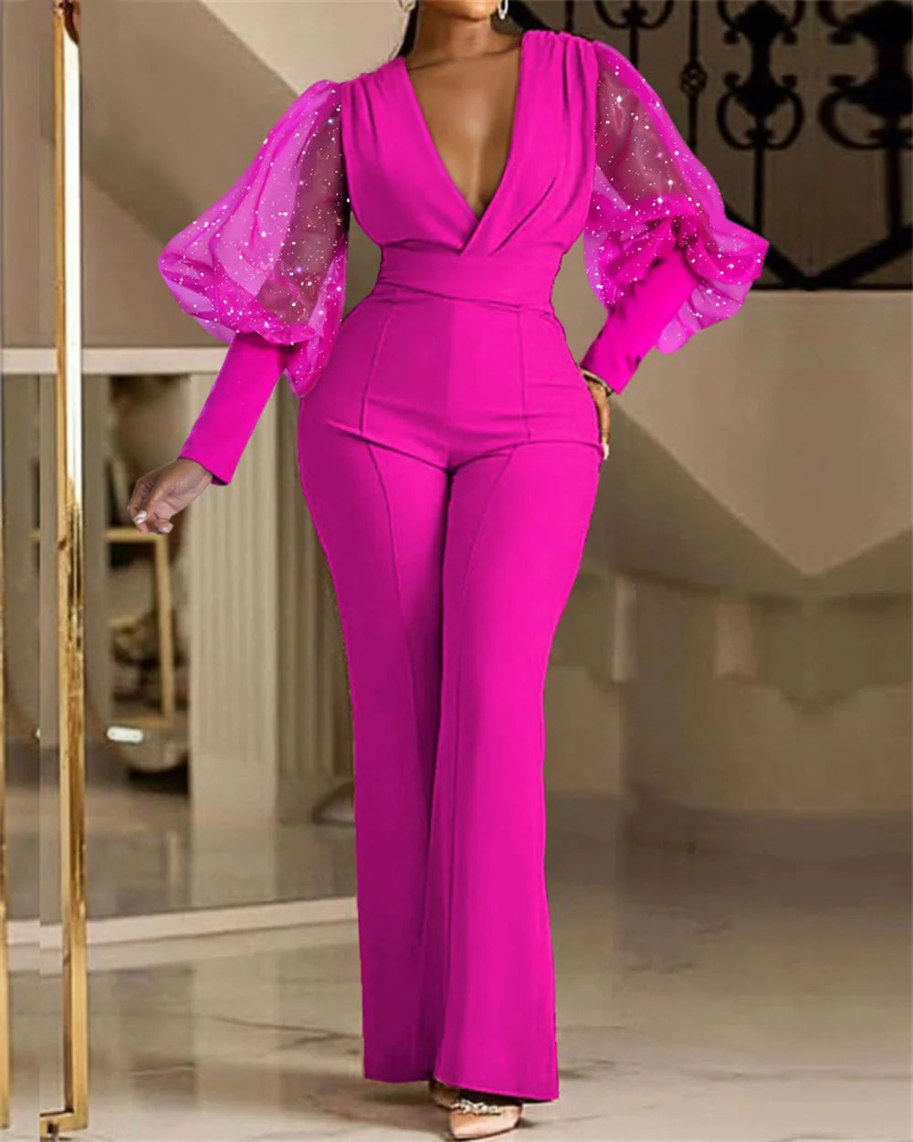 Elegant pink jumpsuit featuring sheer puff sleeves adorned with sparkles, modeled indoors against a staircase backdrop.
