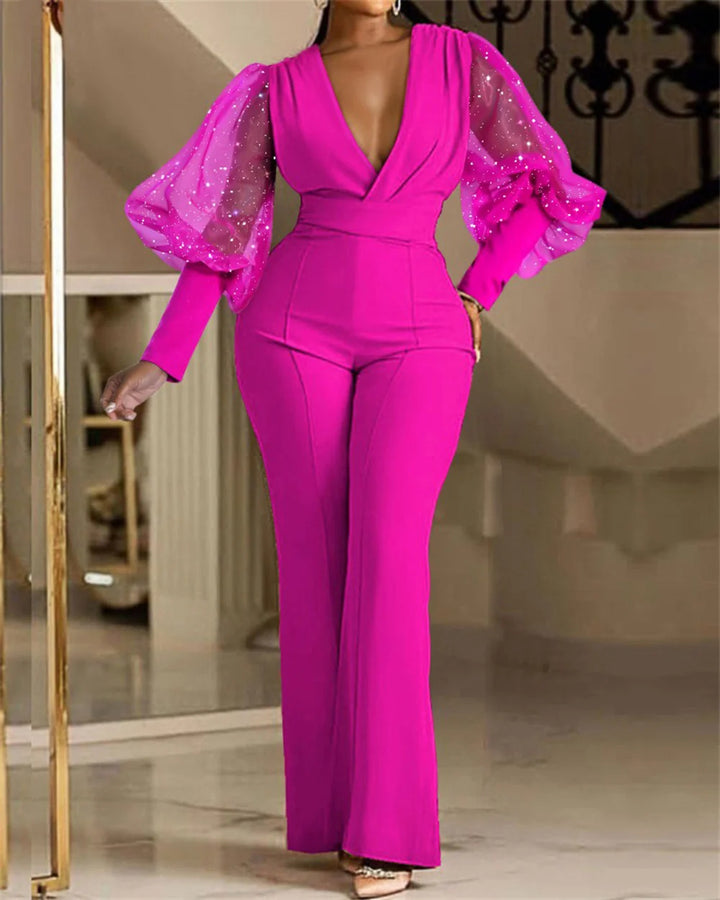 Elegant pink jumpsuit featuring sheer puff sleeves adorned with sparkles, modeled indoors against a staircase backdrop.