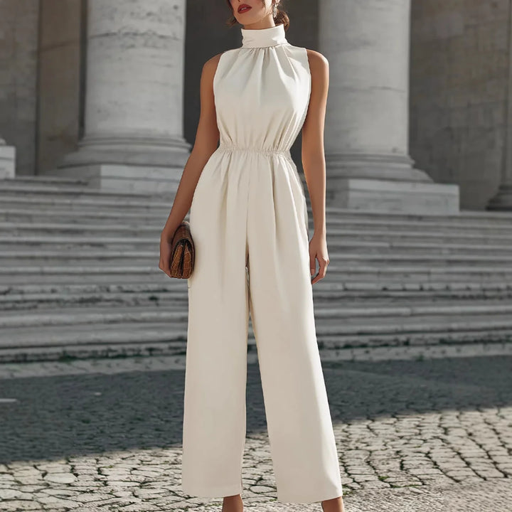 Elegant cream-colored jumpsuit with high collar and cinched waist, showcased in a classic architectural setting with stone steps.