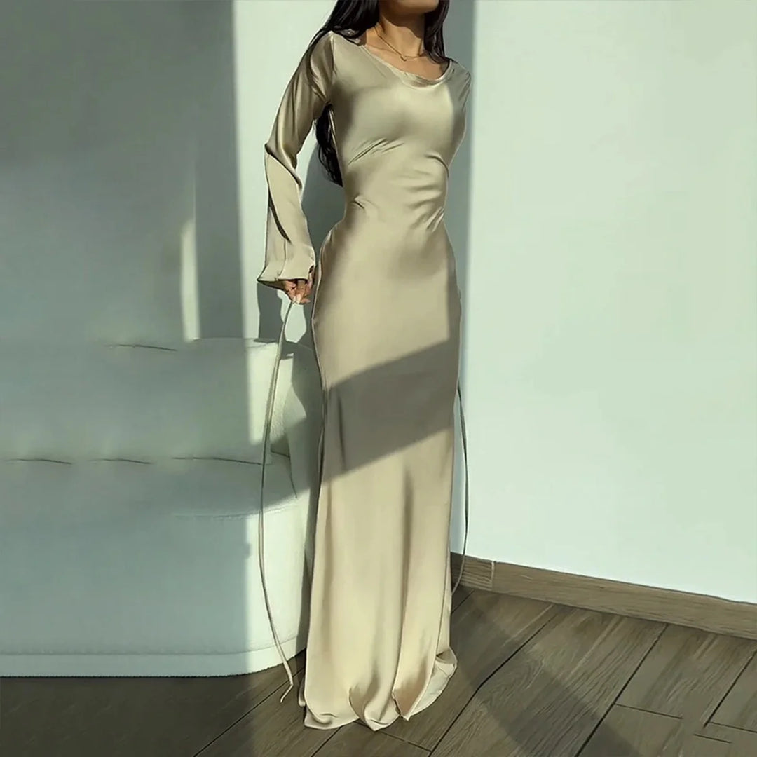 Beige elegant maxi dress with long sleeves, presented in a sunlit room with wooden flooring and a soft sofa.