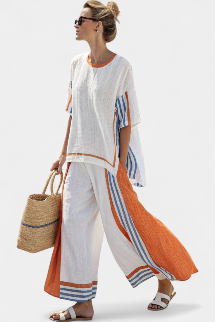 Woman in white two-piece set with orange and blue stripes, holding straw bag, wearing sunglasses against plain backdrop.