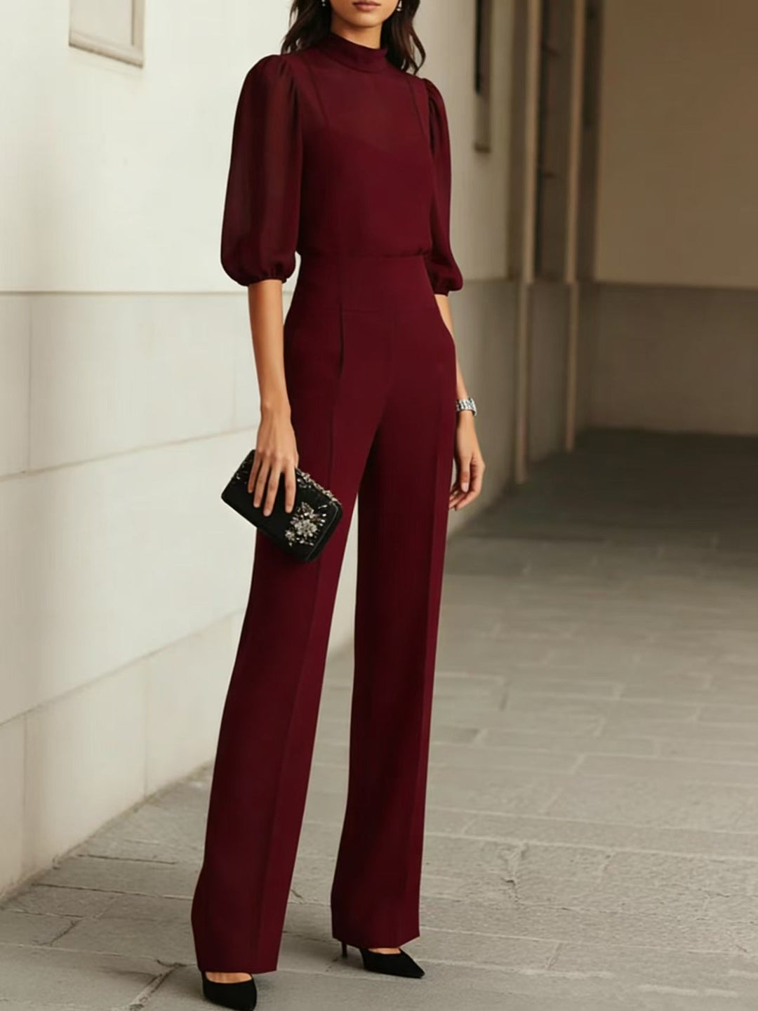 Sophisticated burgundy three-piece set with a sheer blouse and wide-leg pants, accessorized with a clutch, in a refined urban setting.
