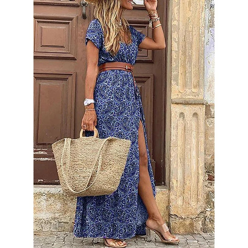 Woman wearing blue patterned dress with slit, holding straw bag, standing by a wooden door.