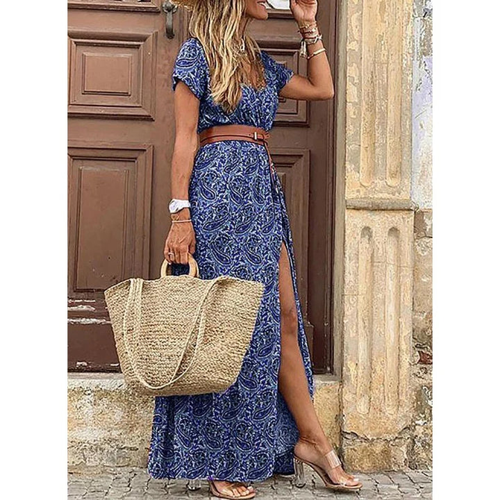 Woman wearing blue patterned dress with slit, holding straw bag, standing by a wooden door.
