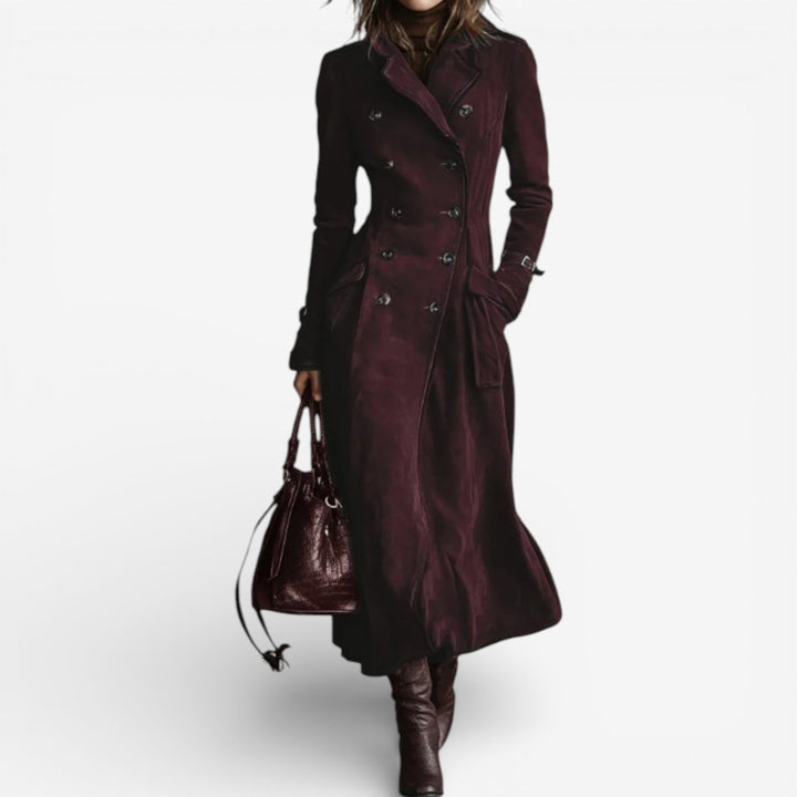 Woman in a long burgundy suede coat with double-breasted buttons, brown boots, holding a matching bag on a white background.