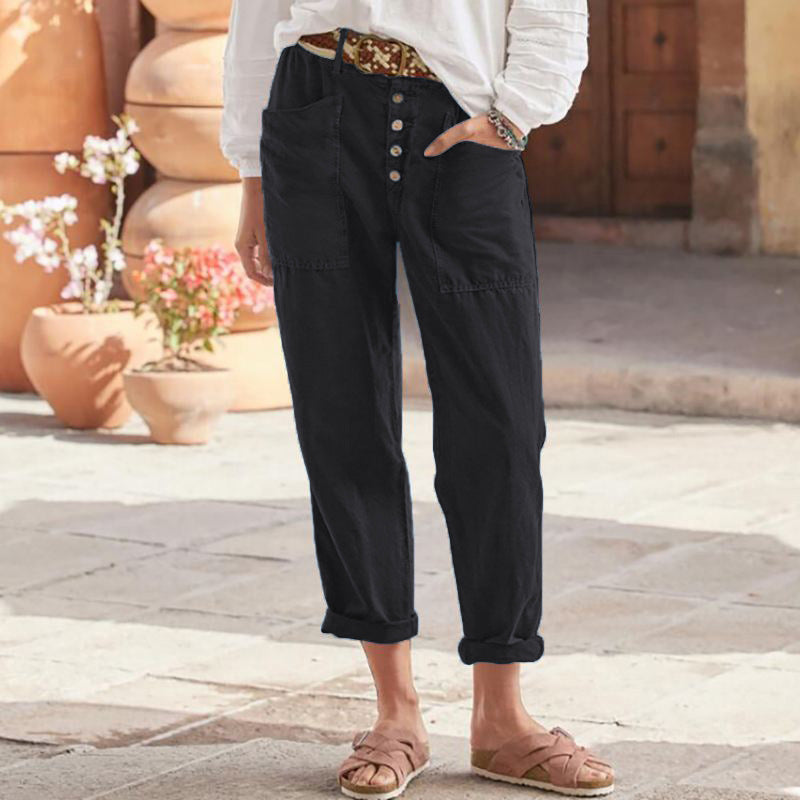 Black casual pants with button front and rolled cuffs, styled with a white top and sandals in a paved area.