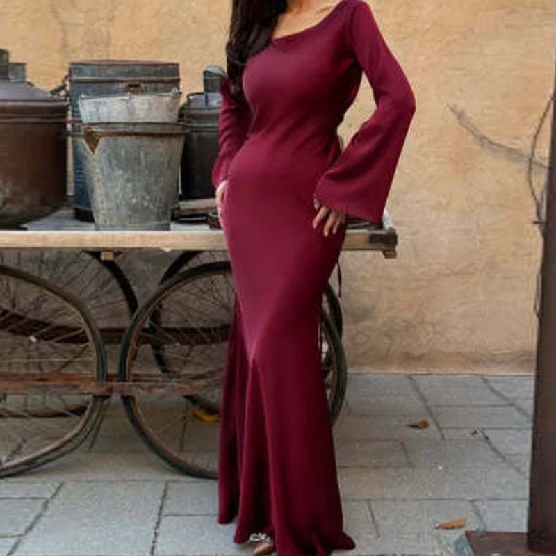 Burgundy elegant maxi dress with long sleeves, showcased in an outdoor setting with vintage barrels and stone paving.