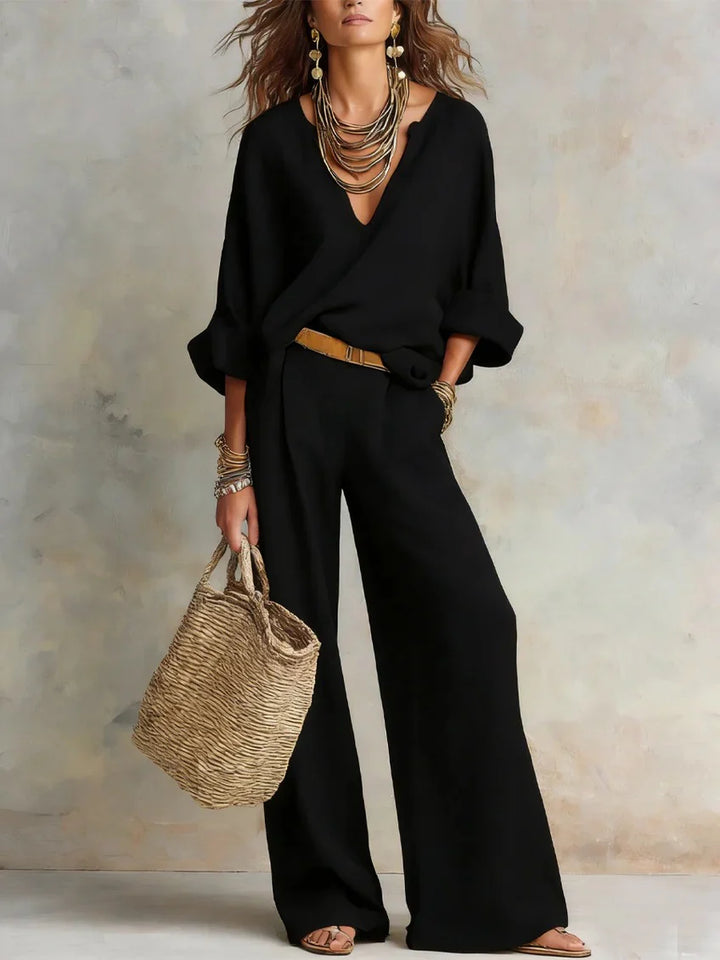 Black two-piece set with statement jewelry and a woven bag, set against a muted studio background.