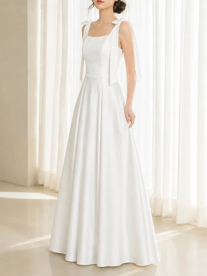 Side view of an elegant white dress with bow straps in a bright room with white curtains.