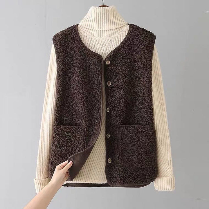 Cozy dark brown sleeveless cardigan with pockets over a cream ribbed turtleneck on a hanger in a plain gray studio.