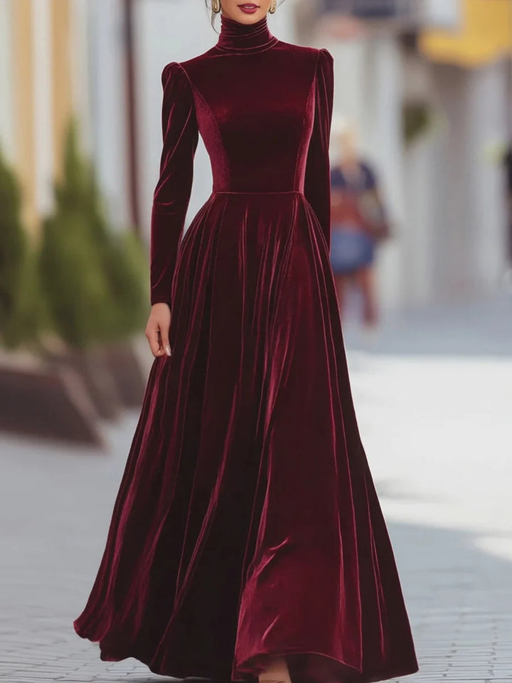 Elegant burgundy velvet dress with long sleeves and a flowing skirt, in a sophisticated urban setting.