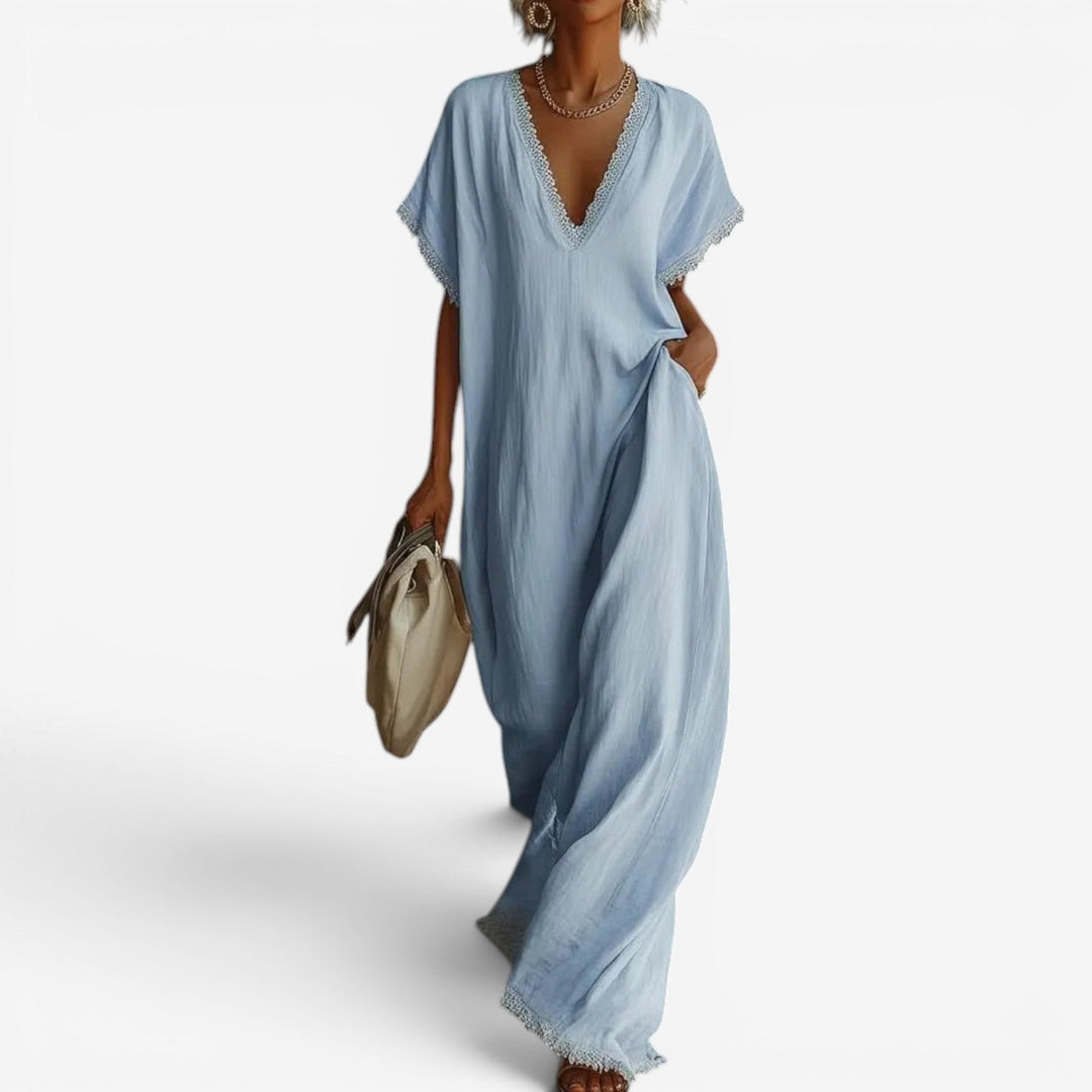 Light blue maxi dress featuring a lace-trimmed V-neckline, worn by a woman holding a beige bag with a plain backdrop.