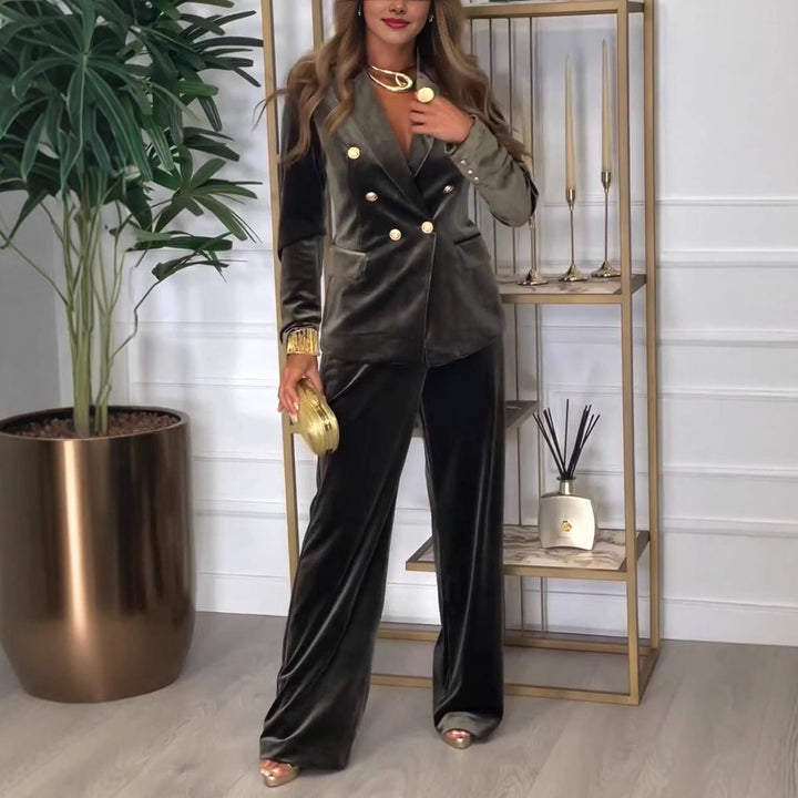 Model wearing an elegant green suit with gold accents, holding a clutch, standing by a decorative golden shelf with candles.