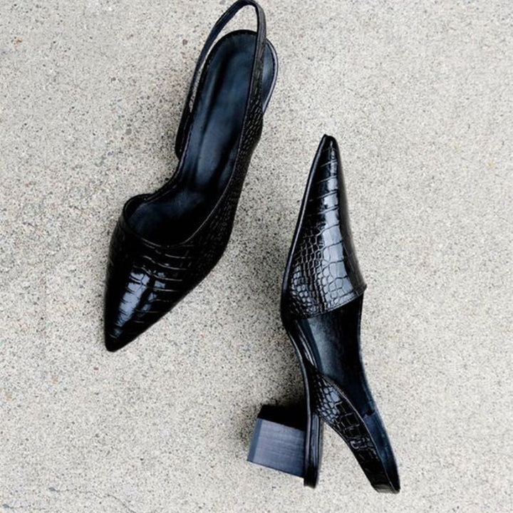 Pair of black orthopedic heels with a shiny, textured finish on a concrete surface.