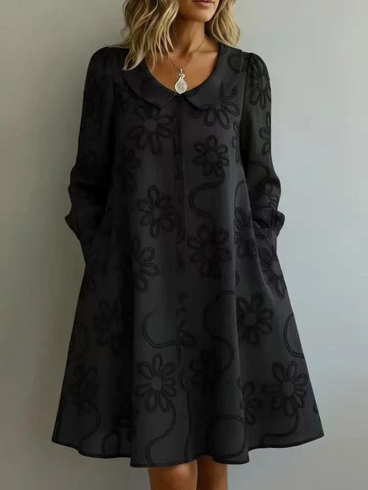 Elegant black midi dress featuring floral embroidery, a collar, and long sleeves in a neutral indoor setting.