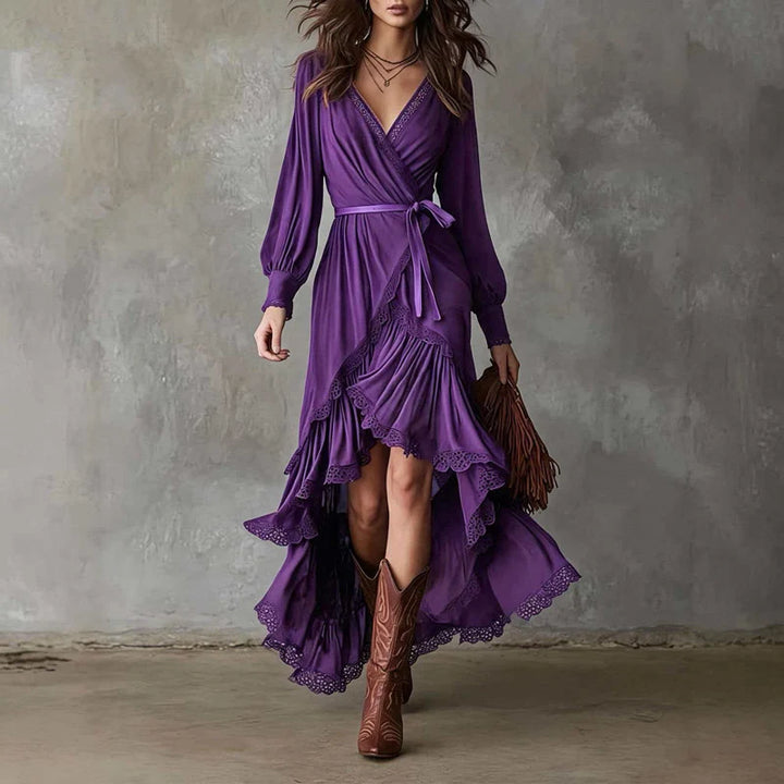 Purple wrap midi dress with ruffled hem, worn with brown boots, against a textured gray wall.
