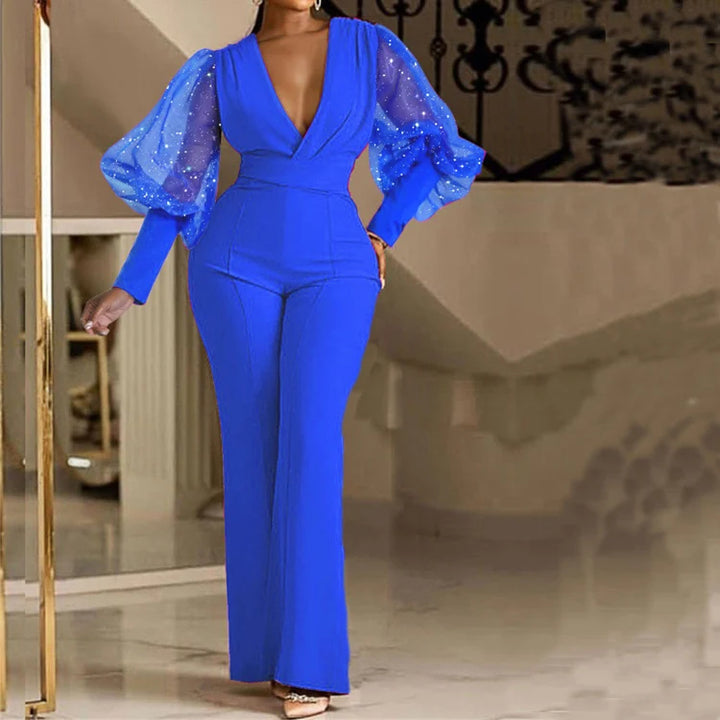 Elegant blue jumpsuit with sparkly sheer puff sleeves, modeled indoors with a staircase backdrop.