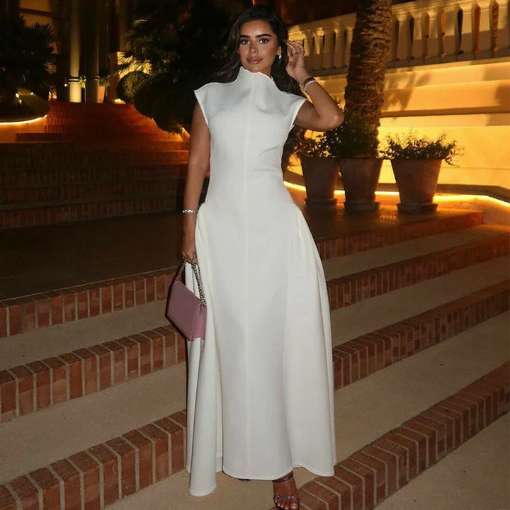 Woman in an elegant white dress on brick steps at night, holding a pink handbag with warm lighting in the background.