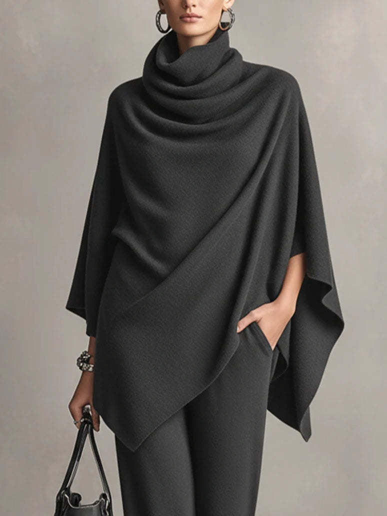 Close-up of black draped top and wide-leg pants in studio setting, showing arm with accessories and handbag.