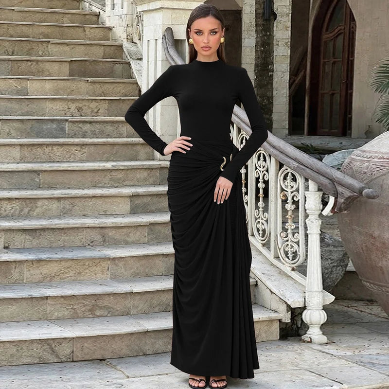 Woman in a black elegant maxi dress with gathered detail, standing on stone steps with ornate railing.