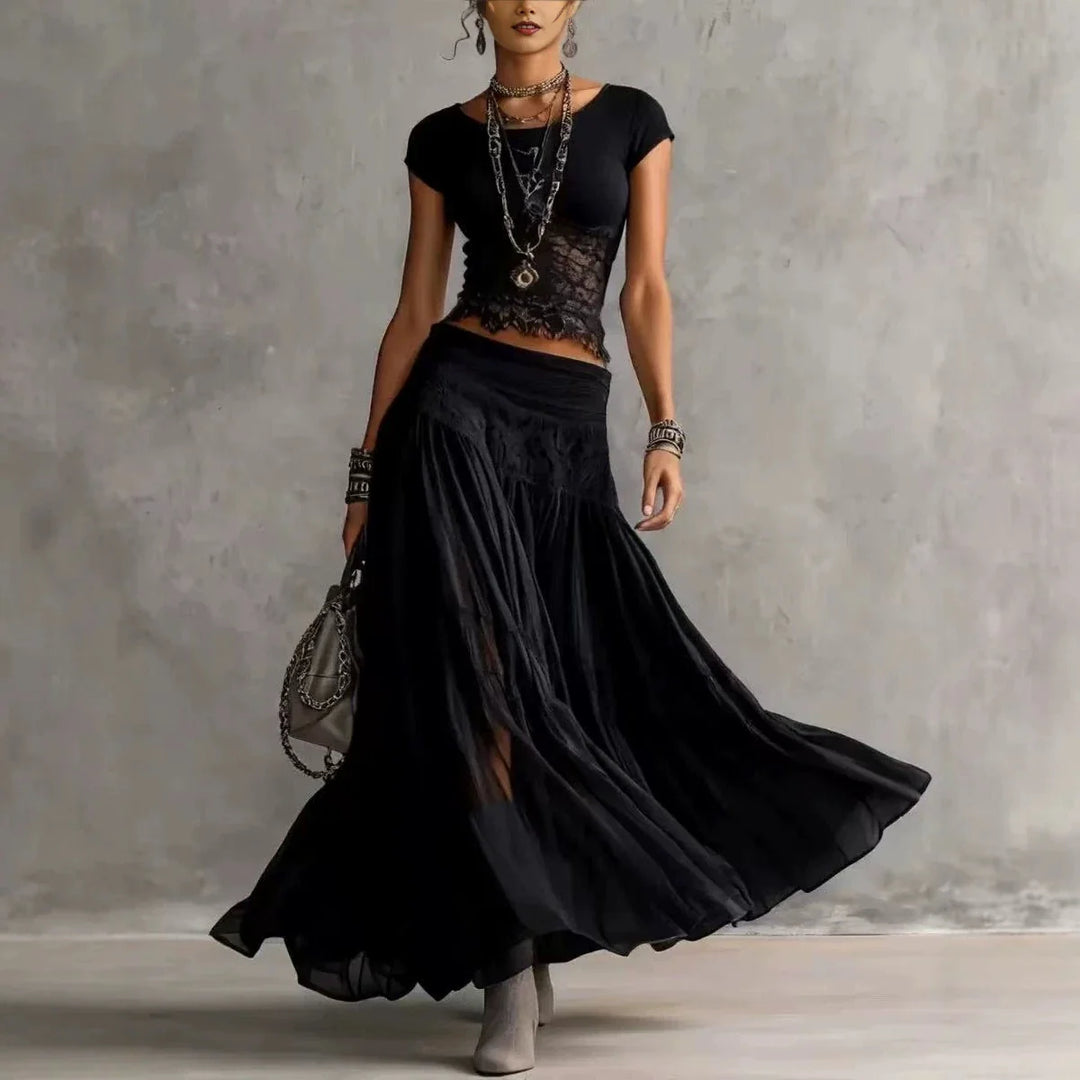 Woman in a black maxi skirt set with lace details, accessorized with layered jewelry, standing in a studio.