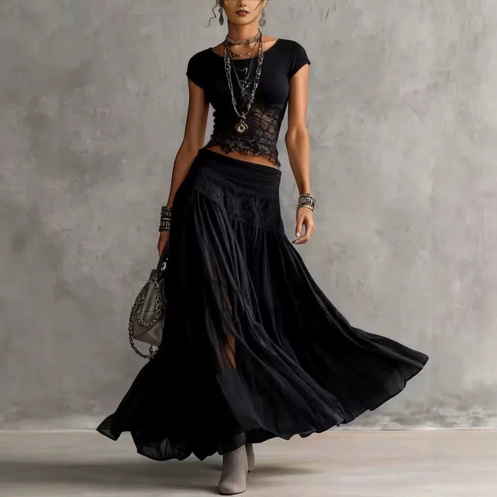 Woman in a black maxi skirt set with lace details, accessorized with layered jewelry, standing in a studio.