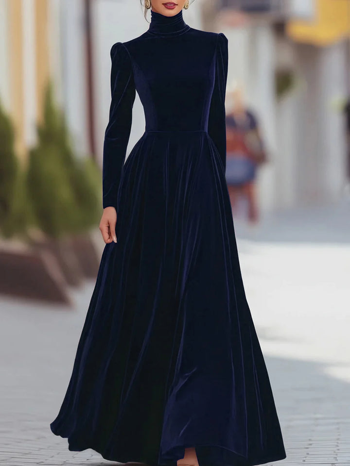 Elegant dark blue velvet dress featuring long sleeves and a flowing skirt, worn in a city backdrop.