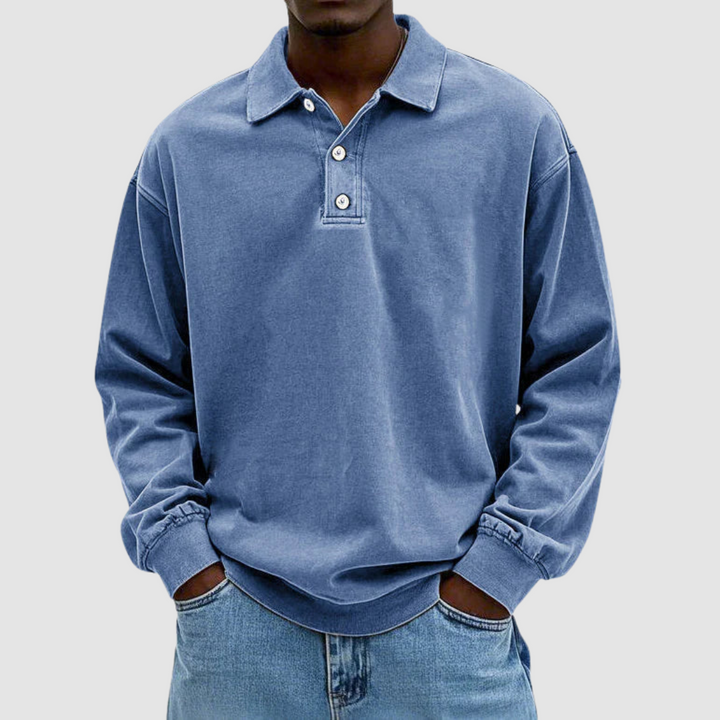 Blue vintage long sleeve polo shirt worn by model, hands in pockets, with light jeans against a plain backdrop.