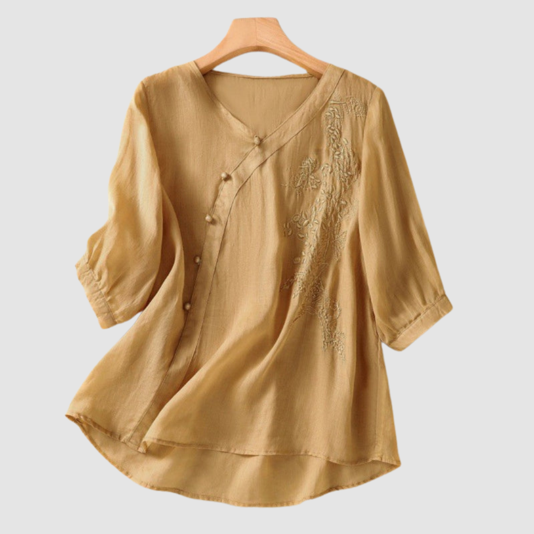 Light mustard blouse with floral embroidery and subtle buttons on hanger against white background.
