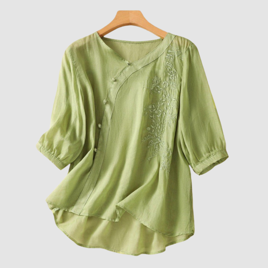 Green blouse with floral embroidery and elegant buttons on hanger against white background.
