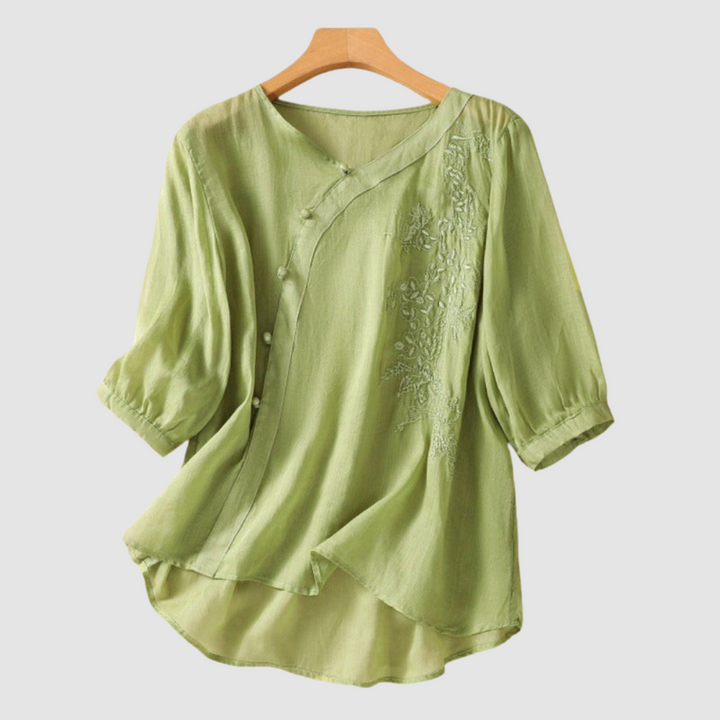 Green blouse with floral embroidery and elegant buttons on hanger against white background.