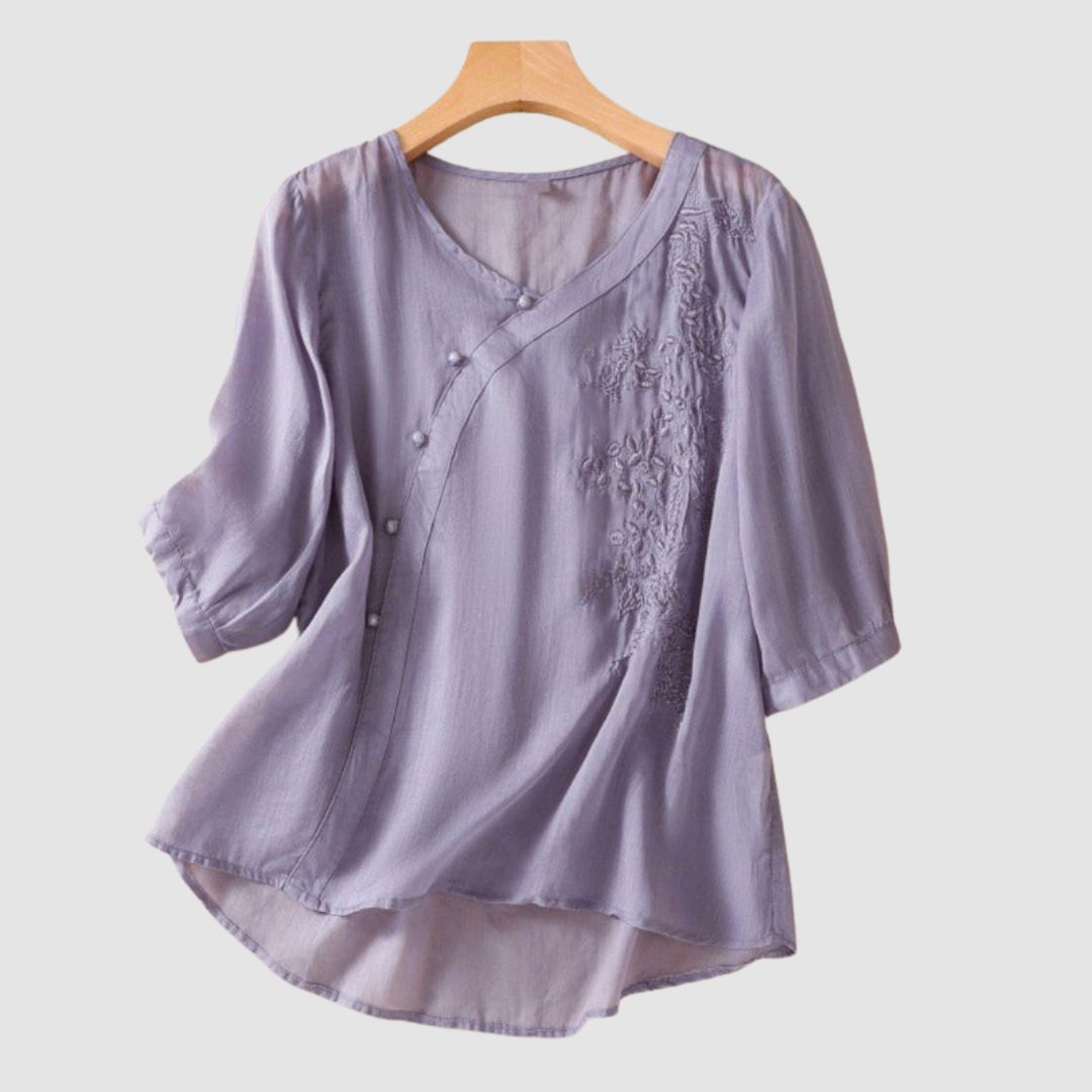 Lavender blouse with floral embroidery and gentle buttons on hanger against white background.
