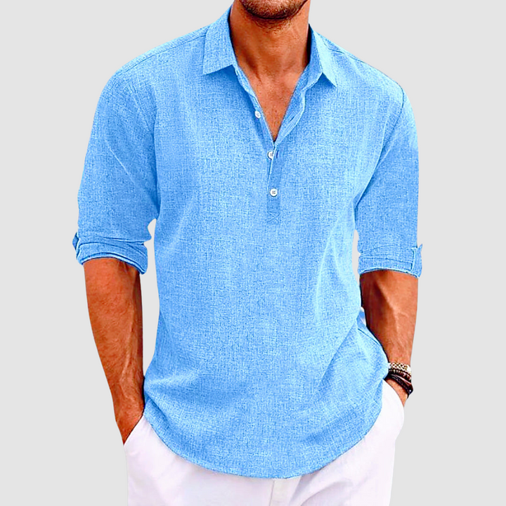 Close-up of a blue collared shirt with rolled up sleeves and buttons, worn by a person with hands in white pants pockets.