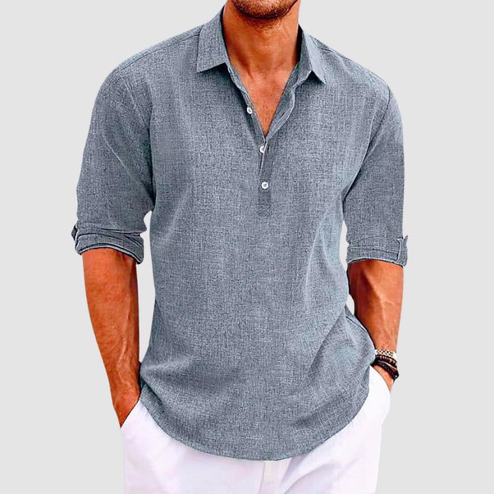 Gray collared shirt with rolled up sleeves and buttons, worn by a person with hands in white pants pockets.