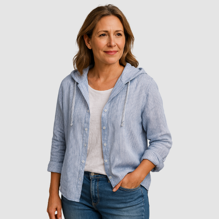 Woman in a light blue striped hooded blouse with white shirt, hands in pocket, studio background.