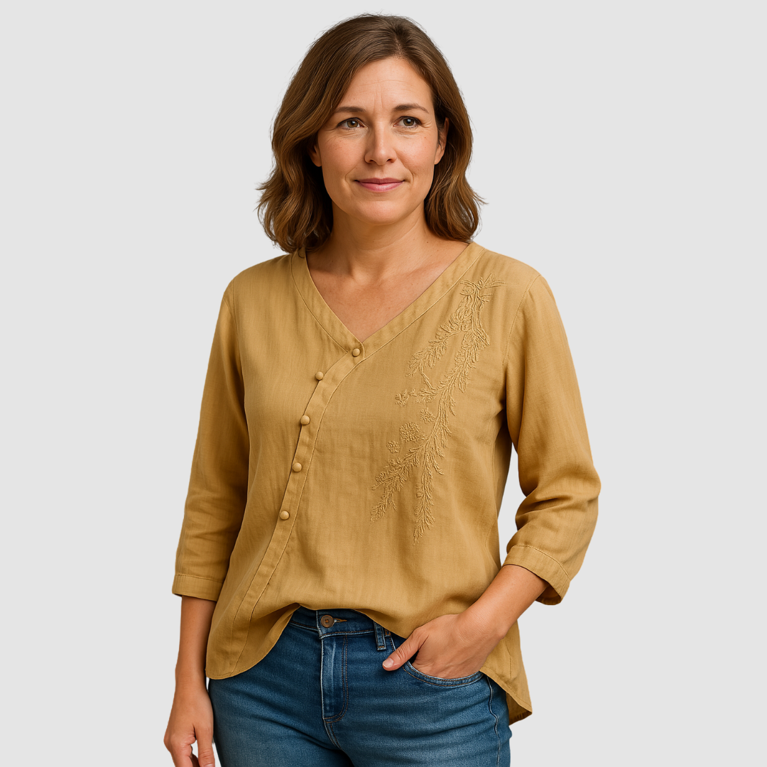 Woman wearing a mustard blouse with floral embroidery and buttons, paired with blue jeans in a studio setting.