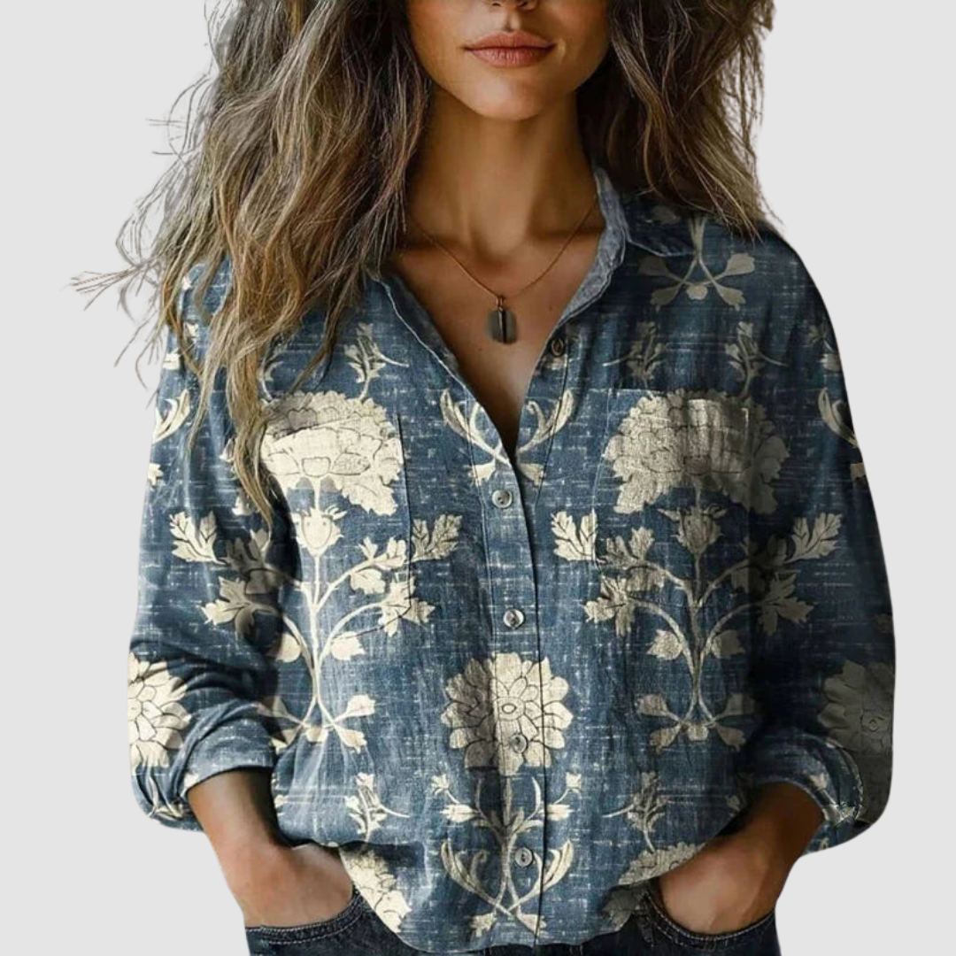 Blue blouse with large beige floral prints, worn by a woman, displayed against a simple background.