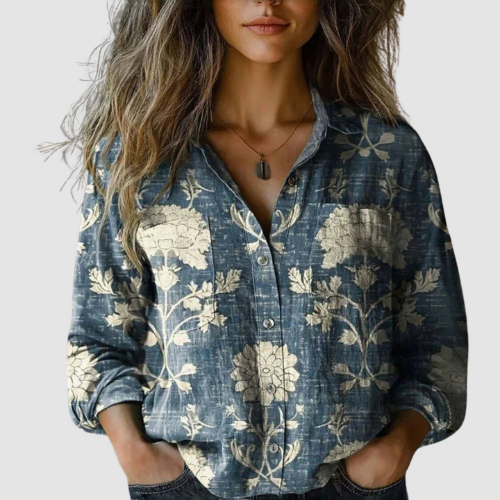 Blue blouse with large beige floral prints, worn by a woman, displayed against a simple background.
