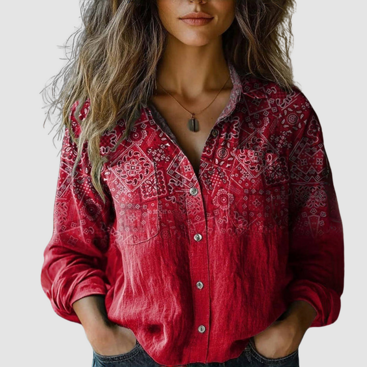 Woman wearing a red blouse with intricate white patterns, buttons down the front, set against a plain background.