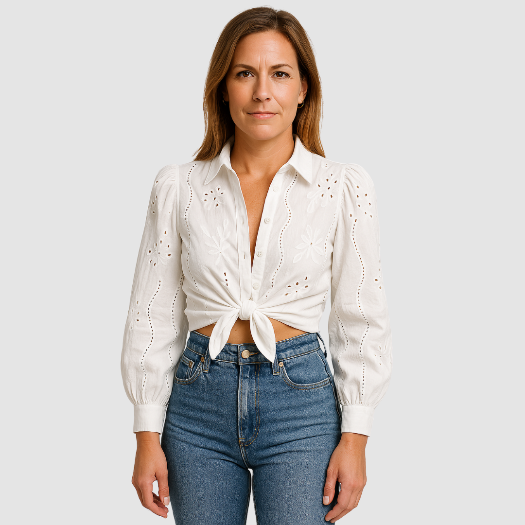 White blouse with floral and eyelet pattern, tied at the waist, worn with blue jeans in a studio.