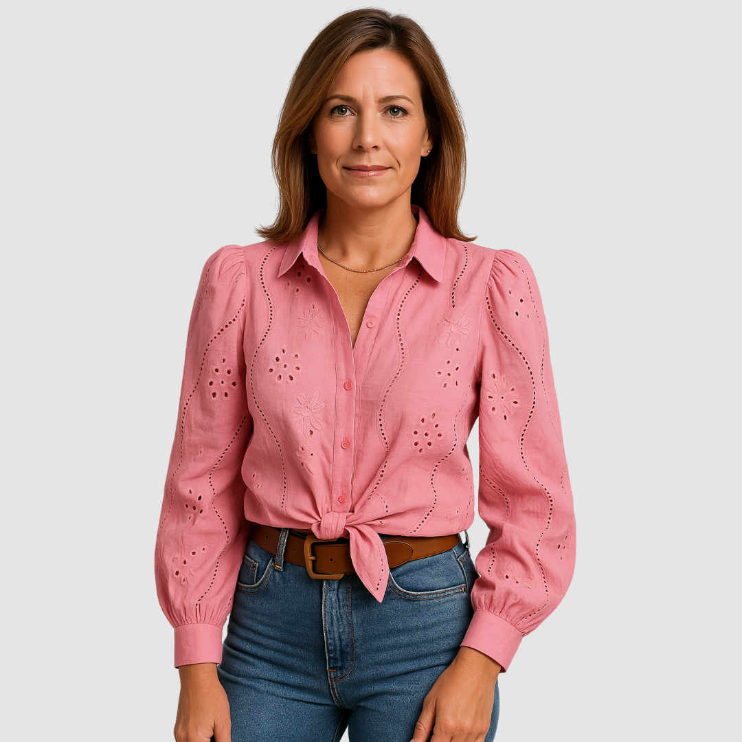 Pink blouse with floral and eyelet details, tied at the waist, paired with blue jeans and brown belt in a studio.