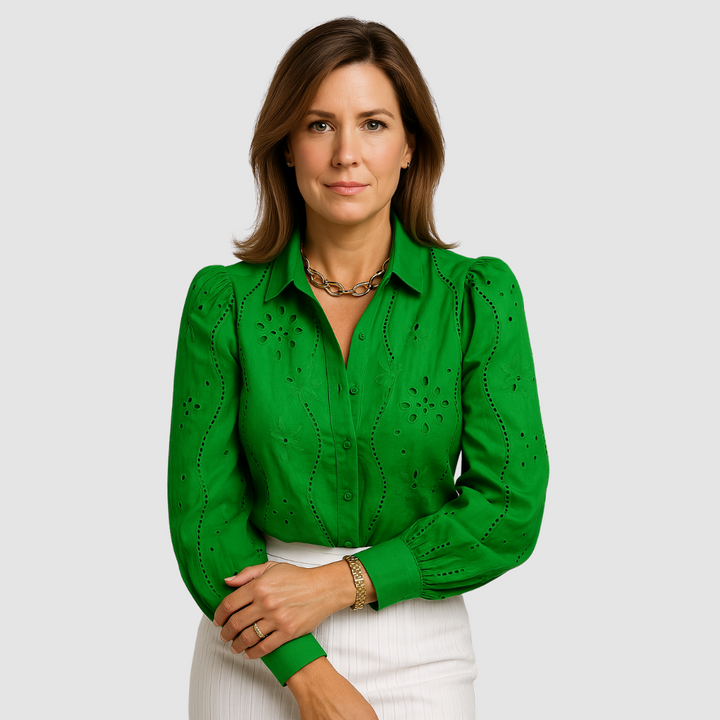 Green blouse with floral and eyelet patterns, buttoned, paired with a white skirt in a studio setting.