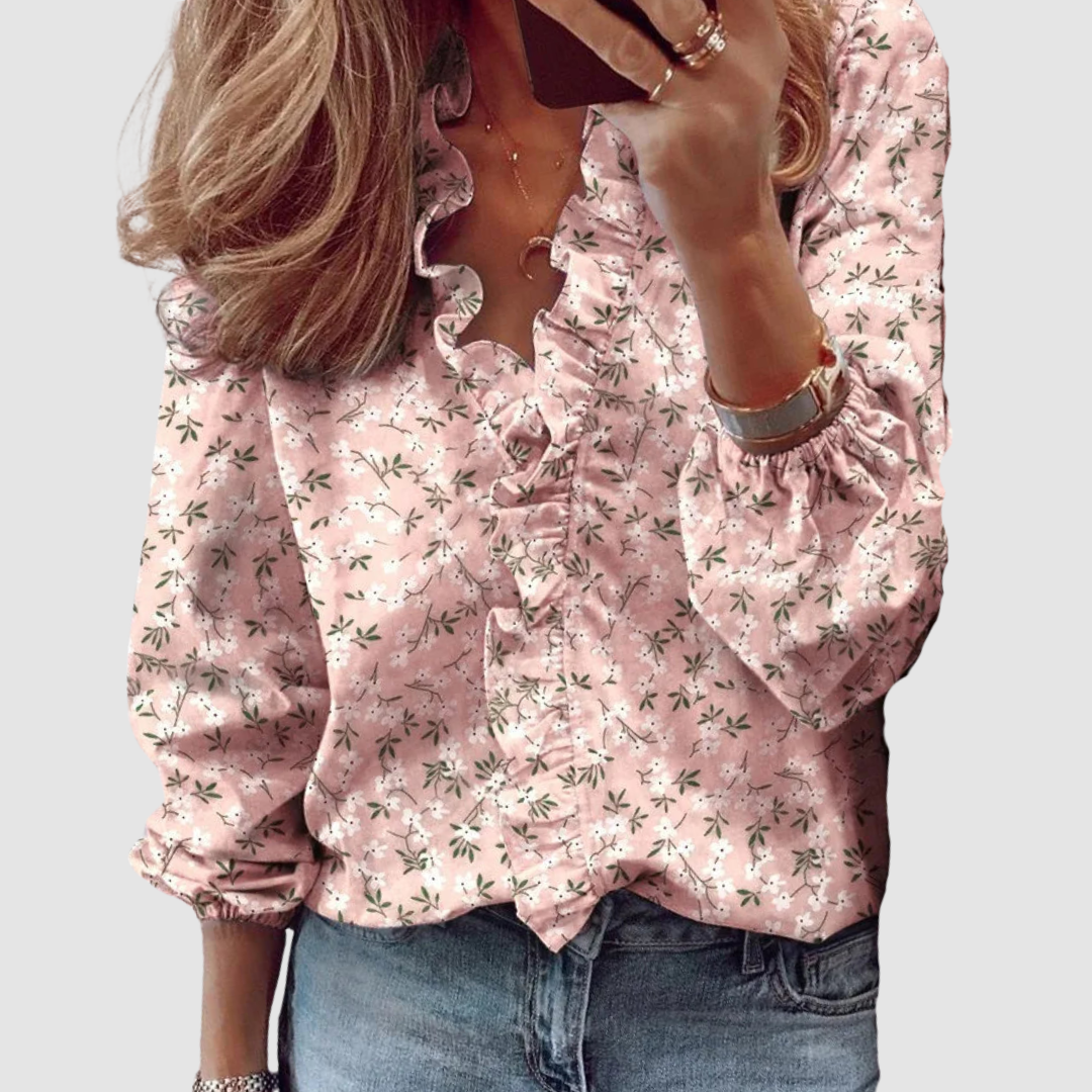 Pink floral blouse with ruffled neckline, worn with jeans in studio setting.