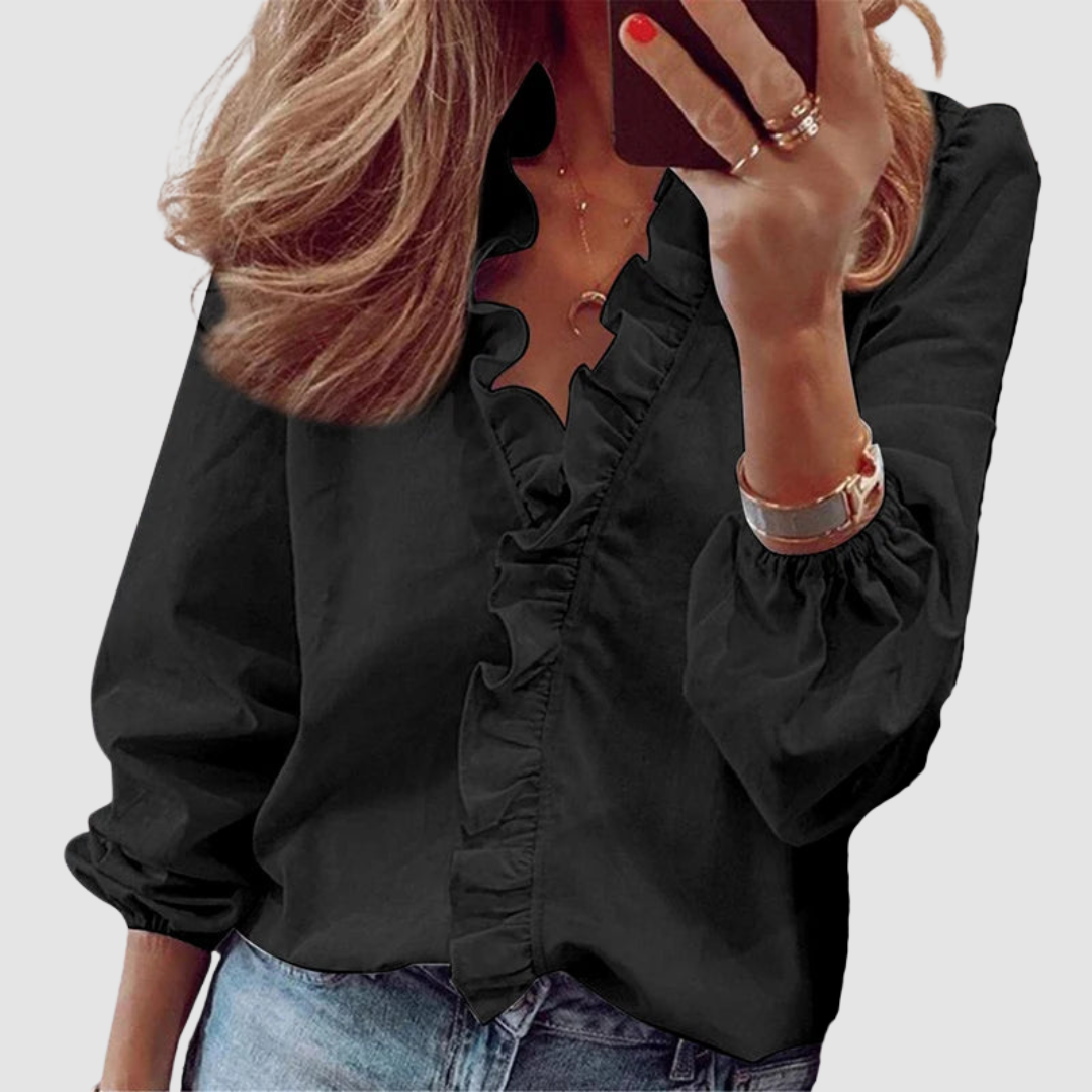 Black blouse featuring ruffled neckline, worn with jeans in studio setting.
