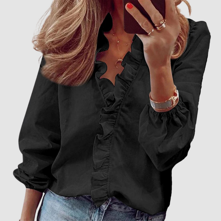 Black blouse featuring ruffled neckline, worn with jeans in studio setting.